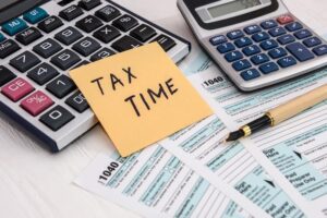 Sticky note that says "Taxes" resting on taxes forms and calculators.