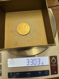 : 1983 Krugerrand being weighed on a digital scale showing 33.03 grams, which is slightly underweight from the standard 33.93 gram specification