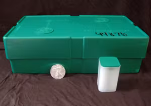 Green cardboard Silver Eagles monster box showing mint markings with individual storage tube and one-ounce coin displayed for size comparison.