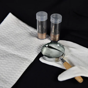Proper silver round handling equipment including clear plastic storage tubes, white cotton gloves, and handheld magnifier for inspection.