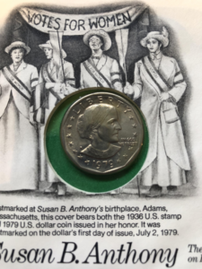 A 1979 Susan B. Anthony dollar mounted on a commemorative first day of issue cover featuring a suffragette illustration and text confirming the coin was postmarked on its release date of July 2, 1979 at Adams, Massachusetts